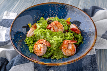 A light, nutritious salad of shrimp, lettuce and olives. Natural delicious food. Greek cuisine menu. Still life in a marine style on a blue background.