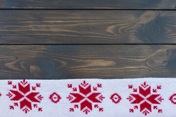 knitted white blanket with traditional christmas pattern with red snowflakes on bottom of dark wooden background. Copy space for text.