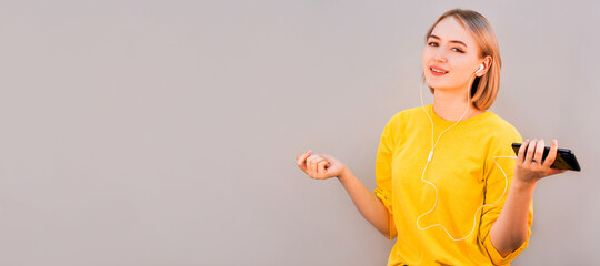 Happy carefree young woman dancing and listening to music from smartphone over grey background