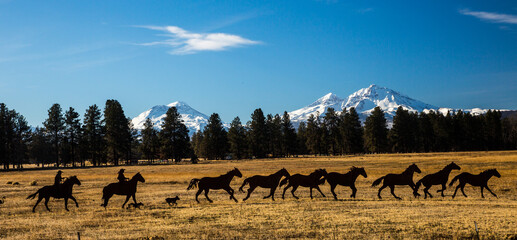 Fototapeta na wymiar Two cowboys are wrangling horses in front of the three sisters mountains, in Central Oregon, The mountains are covered with snow from an early storm