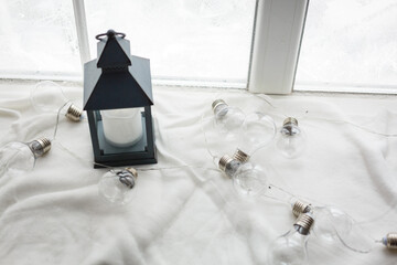 Winter concept. Vintage black lantern with burning candle. Original garland made of lamp bulbs....