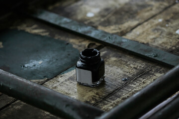 Glass Black ink bottle placed on a dusty grungy wooden plank with metal rods