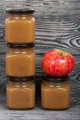 Apple jam in jars. Nearby are ripe apples. On brushed boards, painted black and white.