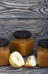 Apple jam in jars. Nearby are apple slices. On brushed boards, painted black and white.
