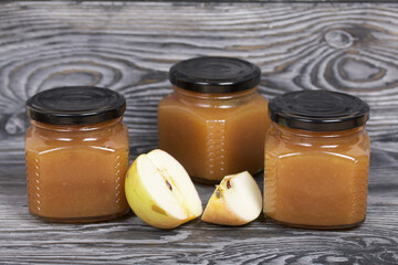 Apple jam in jars. Nearby are apple slices. On brushed boards, painted black and white.