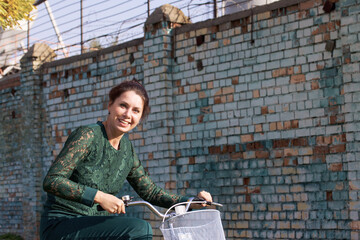 Fototapeta na wymiar The girl in a green tracksuit. Standing, holding the handlebars of the bike. Against the background of a brick wall.