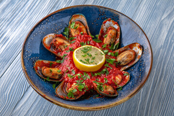 Mussels in a spicy tomato sauce. Natural delicious food. Greek cuisine menu. Still life in a marine style on a blue background.