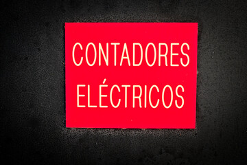 Red warning plate on black background, with text in Spanish (contadores electricos, English translation = electricity meters).
