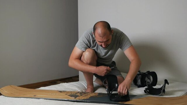 A man attaches bindings to a snowboard at home. Prepares the snowboard for winter