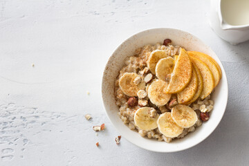 Delicious healthy breakfast. Oatmeal with banana, apple, nuts and cinnamon on a light gray...