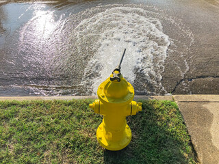 Top view yellow fire hydrant gushing water across a residential street near Dallas, Texas, USA