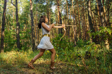 portrait of a young beautiful woman in a white tunic with a bow in the forest in the image of the...