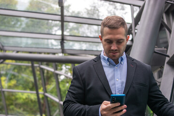 Photo of a young and attractive business man wearing smart casual clothes checking his phone before a meeting. 