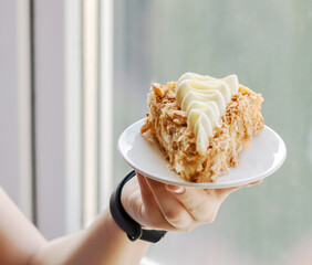 Selective focus to piece of cake with whipped vanilla cream on white plate in child's hand.
