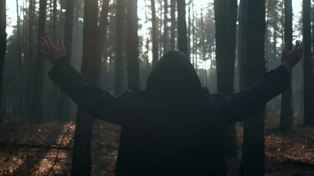 Monk Raising Hands in Prayer. Wanderer Pilgrim in Black Cloak with Cowl Praying in Misty Wood. Autumn Morning. 2x Slow motion 60 FPS