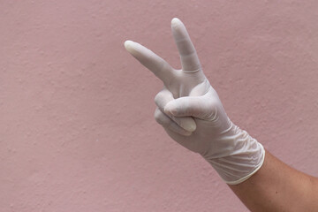 Hand of a person in a white plastic glove gesturing the victory sign