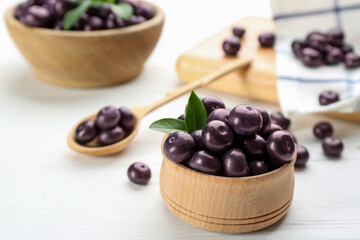 Tasty acai berries in bowl on white wooden table, closeup