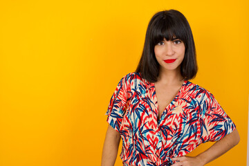 Studio shot of cheerful businesswoman keeps hand on hip, smiles broadly, anticipates for surprise prepared by friends on her birthday, isolated over  background.