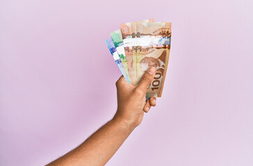 Hispanic hand holding canadian dollars banknotes over isolated pink background.