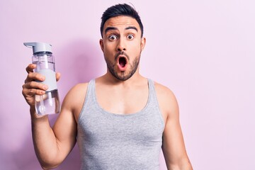 Young handsome sportsman with beard wearing sleeveless t-shirt drinking bottle of water scared and...