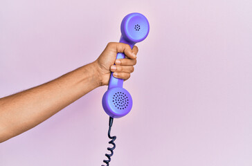 Hispanic hand holding vintage telephone over isolated pink background.