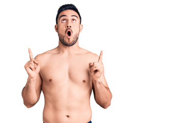 Fototapeta premium Young handsome man wearing swimwear amazed and surprised looking up and pointing with fingers and raised arms.