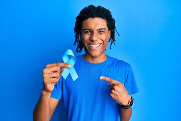 Young african american man holding blue ribbon smiling happy pointing with hand and finger