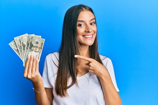 Young hispanic woman holding dollars smiling happy pointing with hand and finger