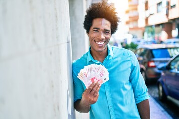 Young african american man smiling happy. Leaning on the wall with smile on face holding israeli...