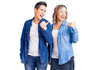 Couple of women wearing casual clothes smiling with happy face looking and pointing to the side with thumb up.