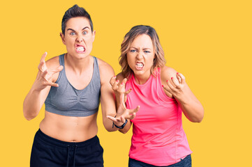 Couple of women wearing sportswear shouting frustrated with rage, hands trying to strangle, yelling mad