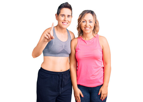 Couple of women wearing sportswear showing and pointing up with finger number one while smiling confident and happy.
