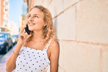 Young beautiful caucasian woman with blond hair smiling happy outdoors speaking on the phone