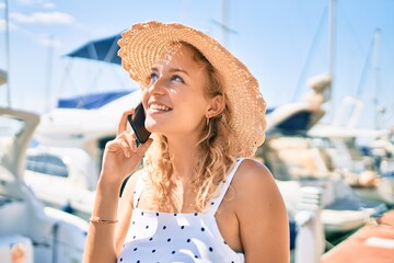 Young beautiful caucasian woman with blond hair smiling happy outdoors speaking on the phone by the nautical port