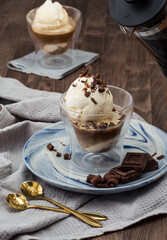 Affogato café. Postre italiano en vaso transparente con helado y cafe. Cucharas doradas en mesa de madera oscura