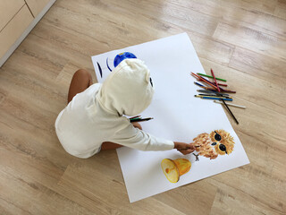 a child sits on the floor and draws a wall paper for school with an owl in pencil