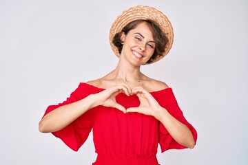 Young hispanic woman wearing summer hat smiling in love doing heart symbol shape with hands. romantic concept.
