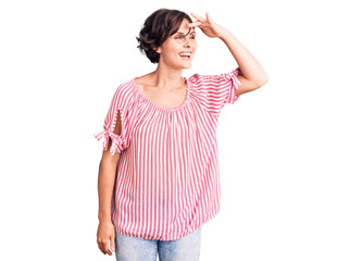 Beautiful young woman with short hair wearing casual summer clothes very happy and smiling looking far away with hand over head. searching concept.