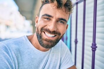 Fototapeta premium Young hispanic man smiling happy leaning on the wall at the city