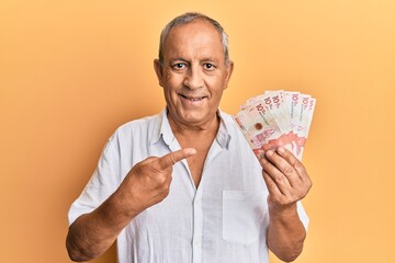 Handsome mature man holding 10 colombian pesos banknotes smiling happy pointing with hand and finger