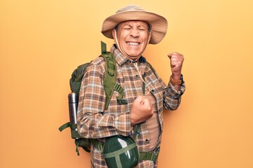 Senior man with grey hair wearing hiker backpack and water canteen celebrating surprised and amazed for success with arms raised and eyes closed