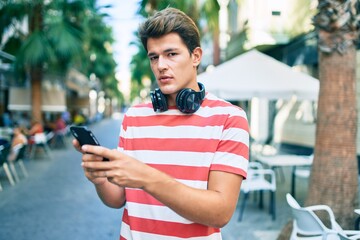 Young caucasian man with serious expression using smartphone and headphones at the city.