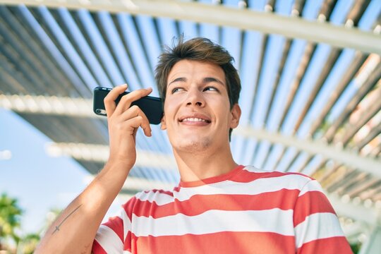 Young caucasian man smiling happy listening audio message using smartphone at the city.