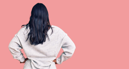 Hispanic woman with long hair wearing casual clothes standing backwards looking away with arms on...