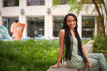 Fototapeta premium Stunning young biracial woman stands on city street in summer - wearing green striped romper