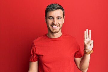 Handsome caucasian man wearing casual red tshirt showing and pointing up with fingers number three while smiling confident and happy.