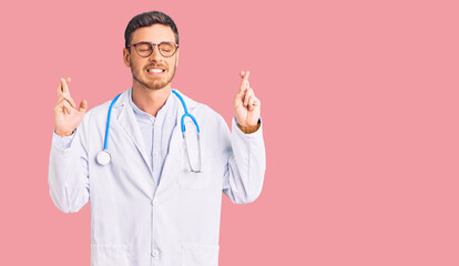 Handsome young man with bear wearing doctor uniform gesturing finger crossed smiling with hope and eyes closed. luck and superstitious concept.