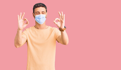 Handsome young man with bear wearing medical mask for coronavirus relax and smiling with eyes closed doing meditation gesture with fingers. yoga concept.
