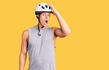 Young handsome man wearing bike helmet surprised with hand on head for mistake, remember error. forgot, bad memory concept.
