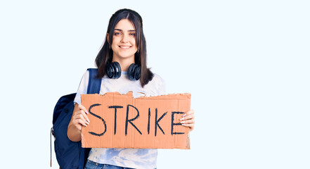 Fototapeta na wymiar Young beautiful girl wearing student backpack holding strike banner looking positive and happy standing and smiling with a confident smile showing teeth